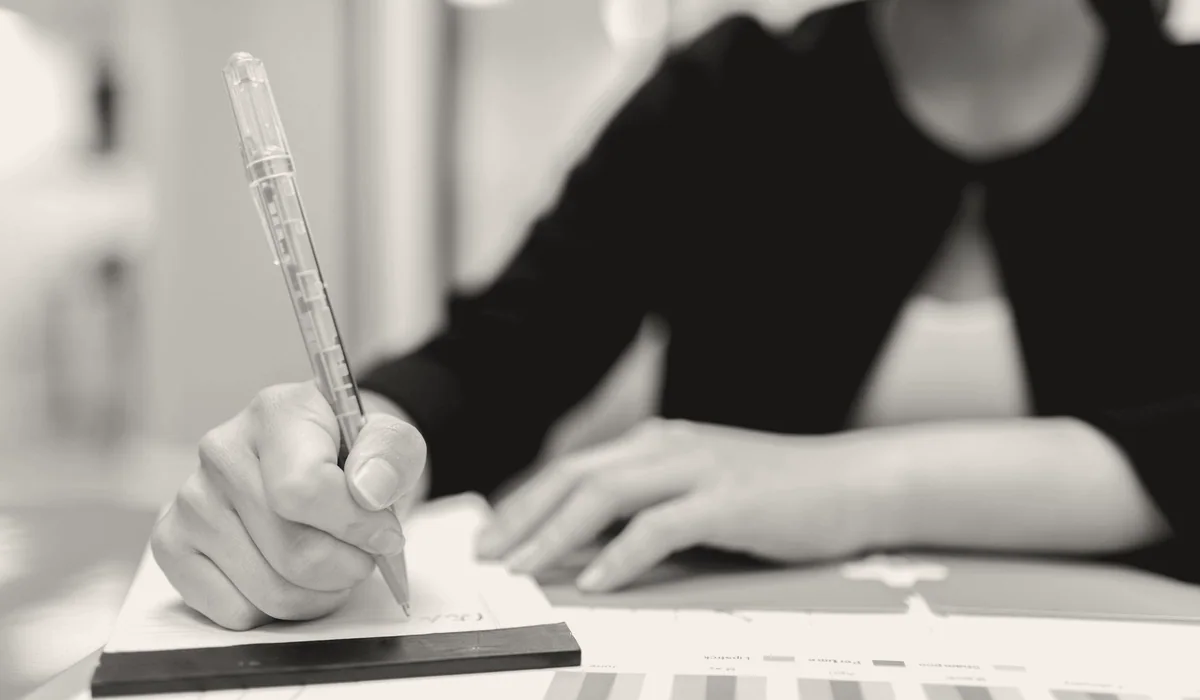 A hand writing notes on a document at a desk.