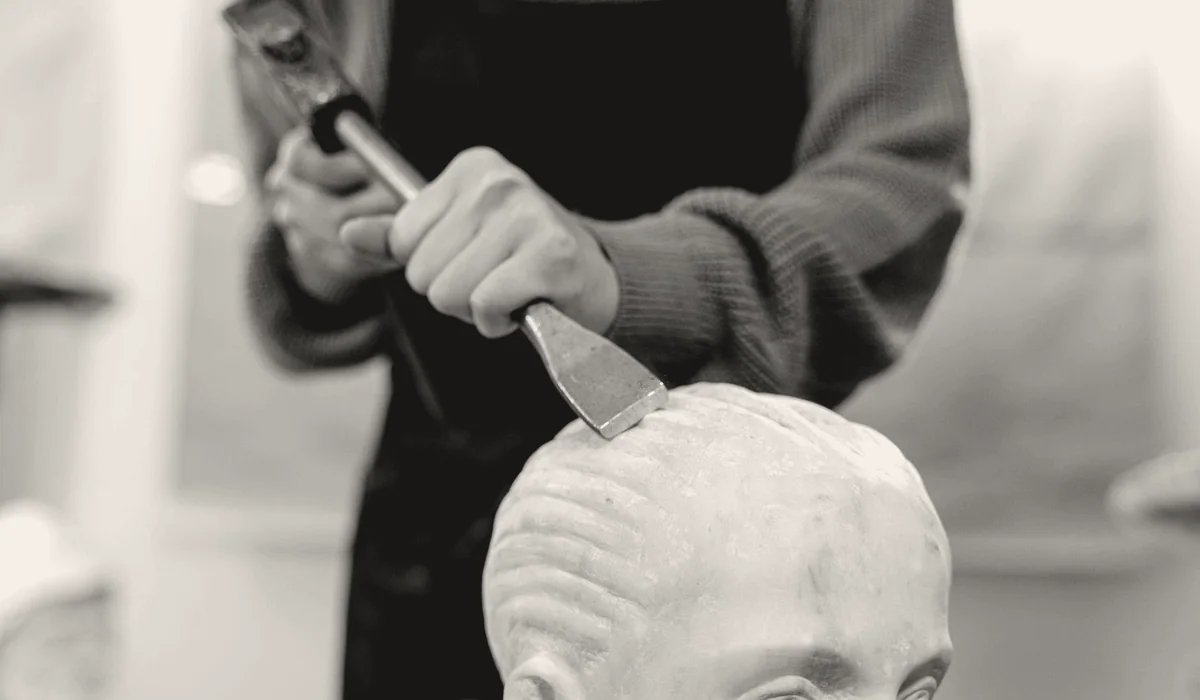 A sculptor carving a stone head with a mallet and chisel.